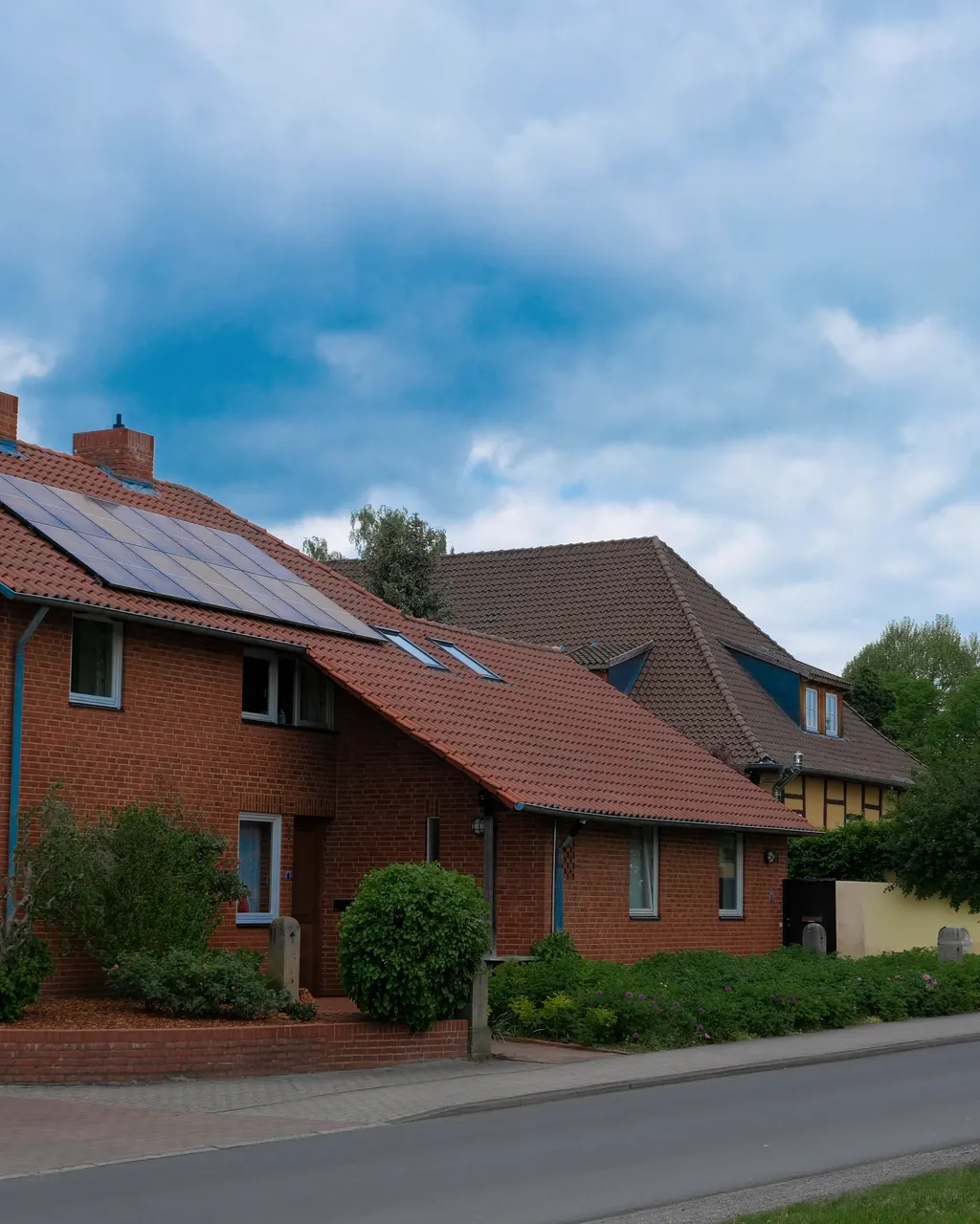 Backsteinwohnhaus mit rotem Ziegeldach und Solarmodulen an einer Wohnstraße